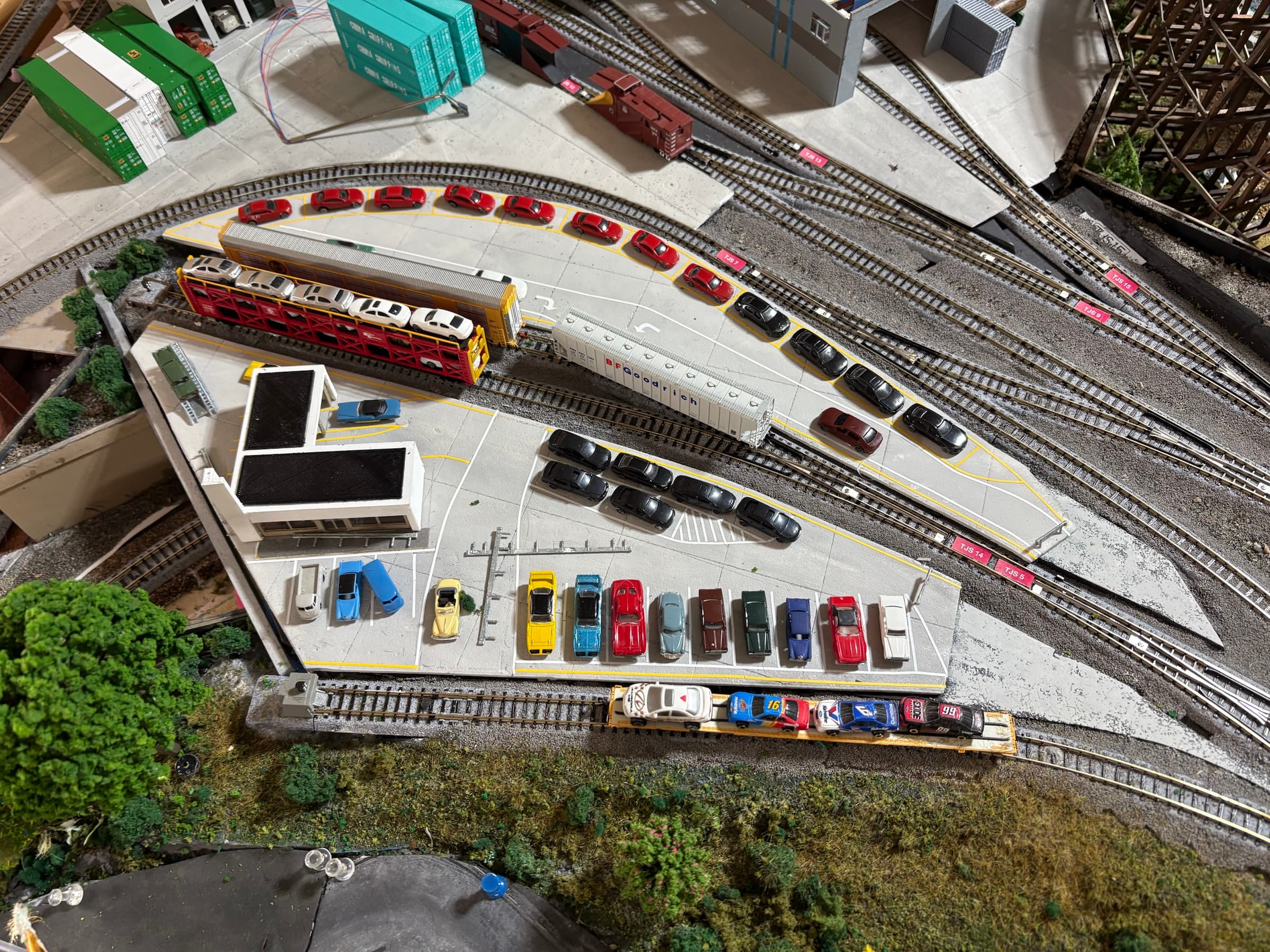 Overhead view of the autorack yard: rows of new cars on the lot beside the tracks and a loaded auto carrier