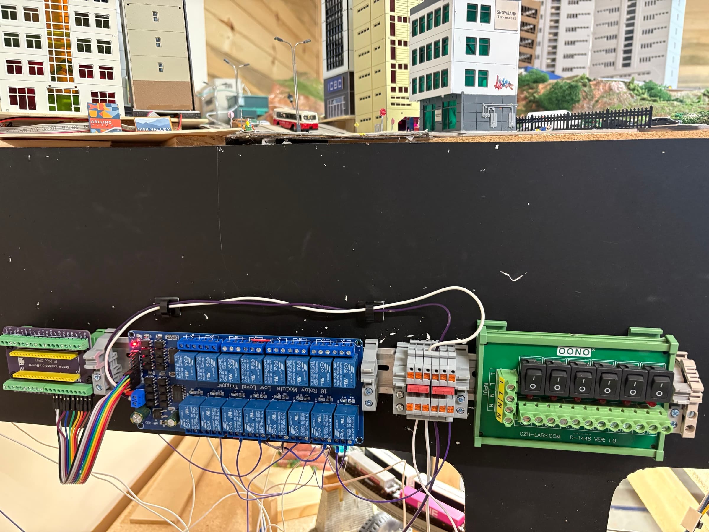 Relay board and terminal board on DIN rail beneath a scenicked city scene